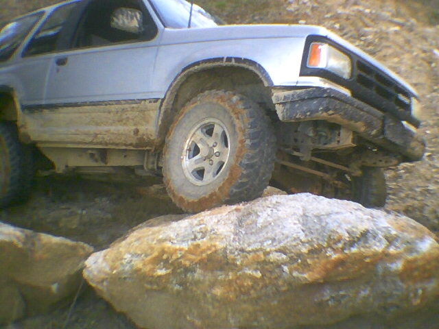 Light blue compact SUV crawling over rocks with muddy body and mud-terrain tires