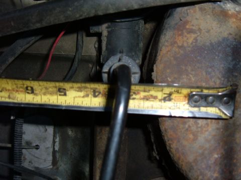 1985 Ford F-150 - A measuring tape is used to measure a component on the underside of a vehicle.