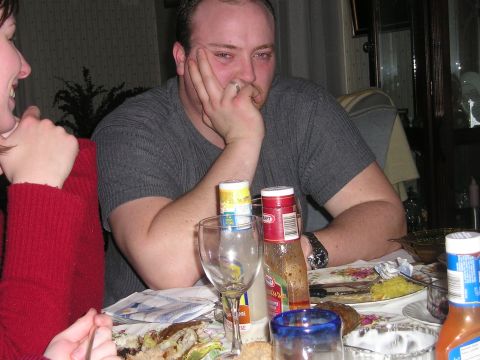 1984 Ford Bronco - A group of people are gathered around a table laden with food and drinks, with one man appearing disengaged from the conversation.
