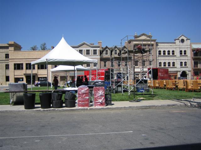 Outdoor event setup with tents, scaffolding, chairs, and buildings