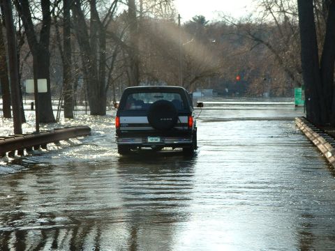 1993 Ford Bronco - A Ford Bronco navigates through deep floodwaters on a road lined with trees.