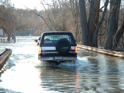 1993 Ford Bronco - A Ford Bronco navigates through flooded terrain, with trees lining the water-covered road.