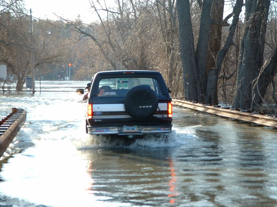 Black Ford Bronco driving through floodwaters, spare tire on rear door