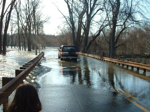 1993 Ford Bronco - A vehicle navigates a flooded road, with water covering the pavement and surrounding areas.