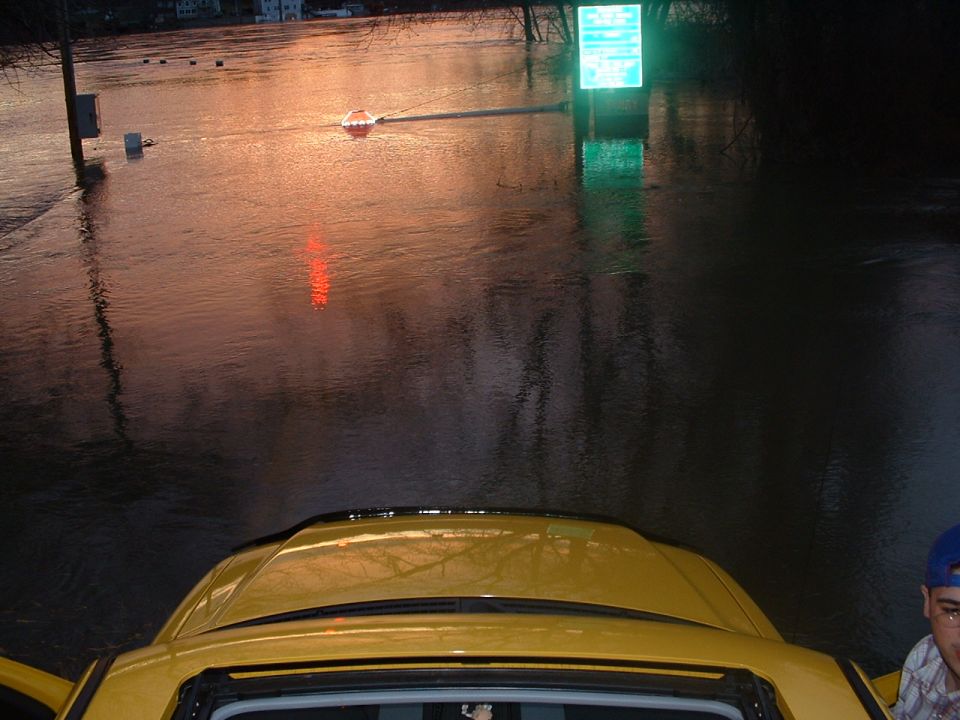 Yellow SUV interior view, submerged in floodwater, with a glowing green sign in the background