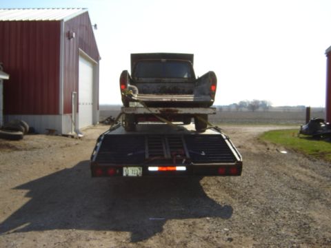 1992 Ford Bronco - Pickup truck loaded onto a trailer, parked near a red barn.