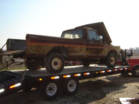 1992 Ford Bronco - A weathered Ford F-Series pickup truck is transported on a flatbed trailer, showing its age and wear.