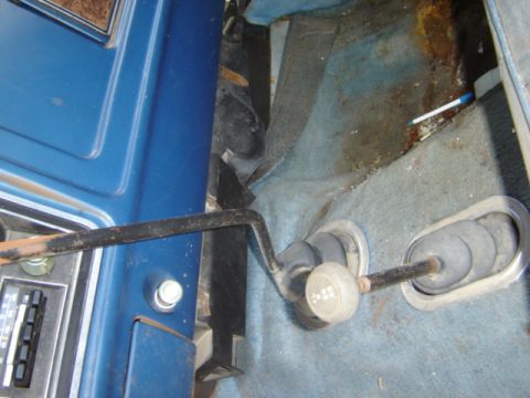 1992 Ford Bronco - The interior of a vehicle shows a floor shifter and worn blue carpet with rust stains.