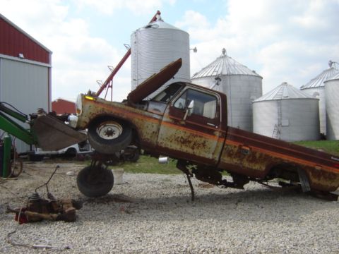 1992 Ford Bronco - A heavily rusted pickup truck is being worked on, with its front end lifted by a loader.
