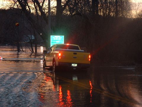 1993 Ford Bronco - A yellow pickup truck navigates through flooded roads during sunset, with a digital sign illuminated ahead.