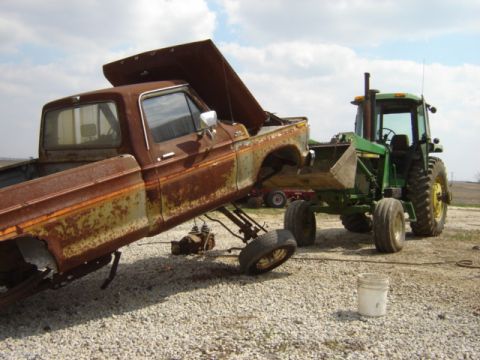 1992 Ford Bronco - Old Ford pickup truck being loaded onto a tractor in a gravel yard.