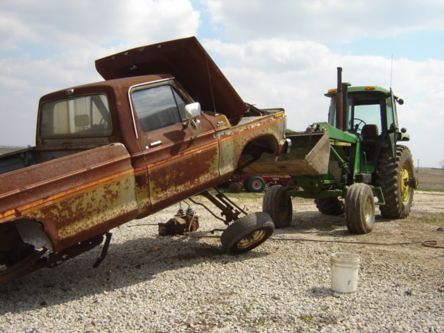 Rusty 1979 Ford F-Series pickup truck with hood open, being loaded onto a green tractor