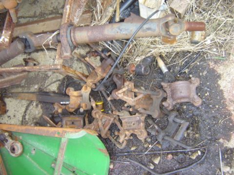 1992 Ford Bronco - A collection of various rusty vehicle components are scattered on the ground amidst debris.
