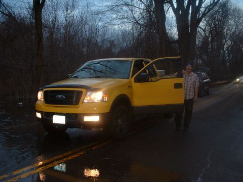 1993 Ford Bronco - Yellow Ford F-150 pickup truck with driver's door open, parked on wet road next to trees.
