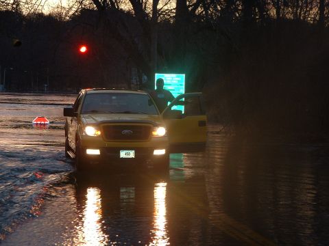 1993 Ford Bronco - A yellow Ford F-150 navigates through flooded streets as dusk settles, with a person standing near the open door.