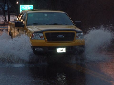 1993 Ford Bronco - Yellow Ford F-150 truck driving through flood water, creating large splashes.