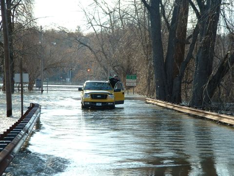 1993 Ford Bronco - Yellow Ford F-150 pickup truck navigates flooded road with driver's door ajar.