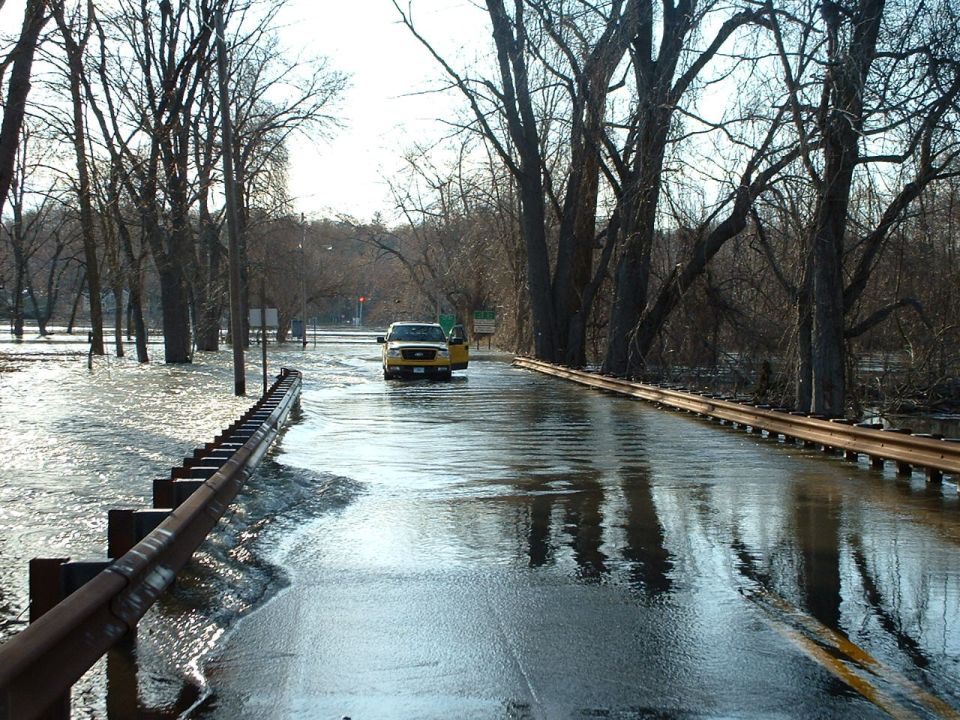 Yellow pickup truck driving on a flooded road with trees on the side