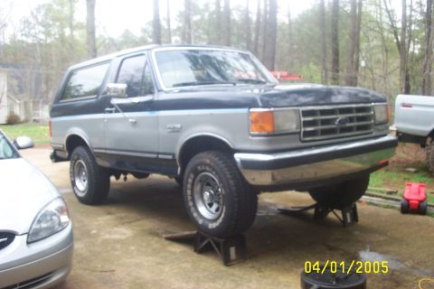 1979 Ford F-150 - This two-tone Ford Bronco is elevated on jack stands, with another vehicle visible to the left and rear.