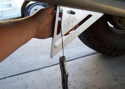 1994 Ford F-150 - A speed square and plumb bob are used to measure the vehicle's frame, likely for alignment or modification purposes.