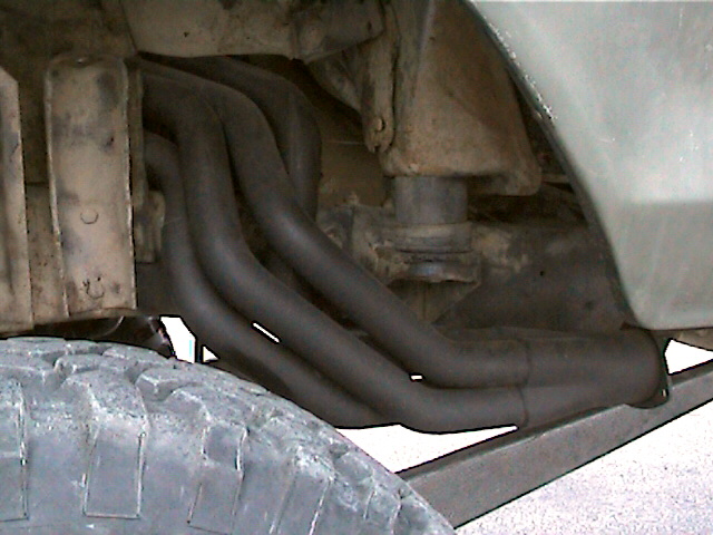 Underbody view of long-tube headers running down from cylinder head behind a tire