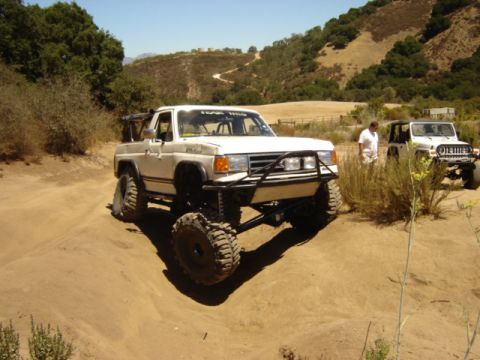 1991 Ford Bronco - Two off-road vehicles navigate a dusty trail on a sunny day.