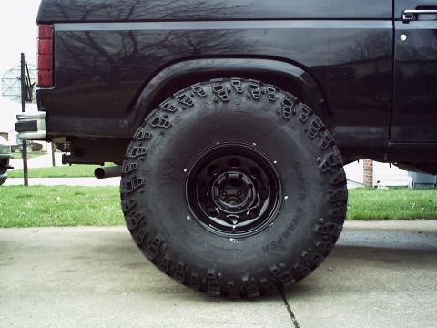 1986 Ford Bronco - Close-up of the rear wheel and fender of a black SUV, showing off-road tires.