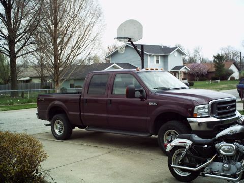 1986 Ford Bronco - A maroon Ford F-250 Super Duty pickup truck is parked on a concrete driveway with a motorcycle in the foreground.