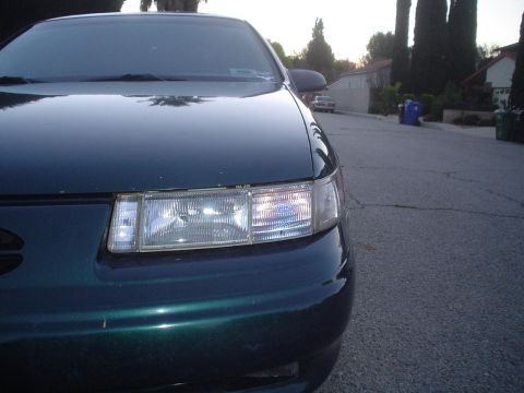 1993 Ford Taurus - Dark green sedan's front end with headlights illuminated, parked on a residential street.