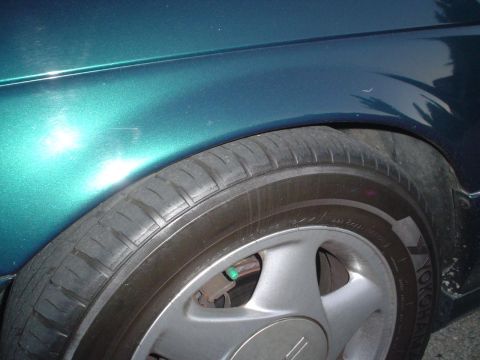 1993 Ford Taurus - Close-up view of a green car's fender and tire, showing the wheel and part of the brake caliper.