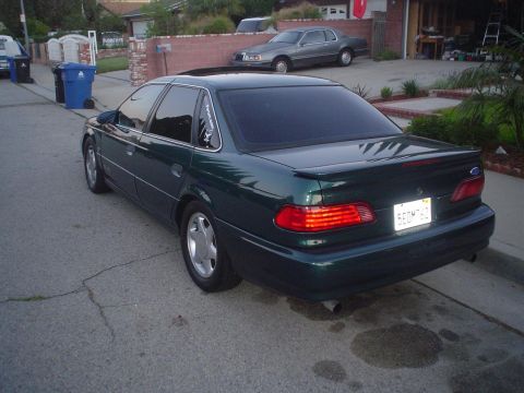 1993 Ford Taurus - A dark green 1993 Ford Taurus is parked on a residential street, showing its rear end and a spoiler.