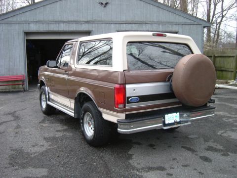 1993 Ford Bronco - This two-tone Ford Bronco is viewed from the rear, parked on asphalt in front of a garage.