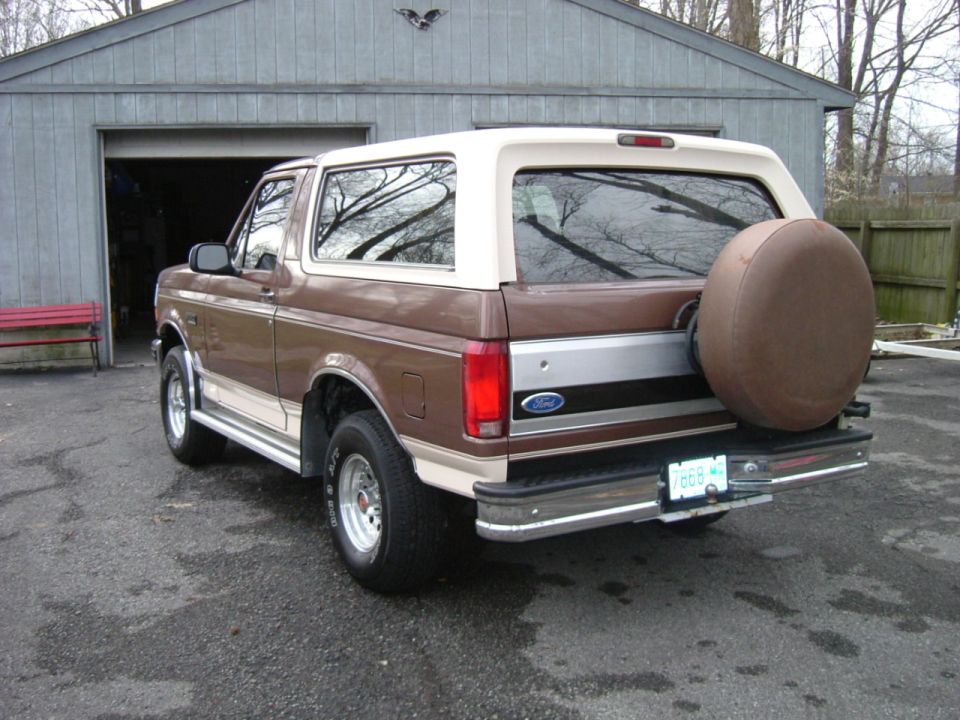 Brown and tan 1990s Ford Bronco, rear three-quarter view, with covered spare tire