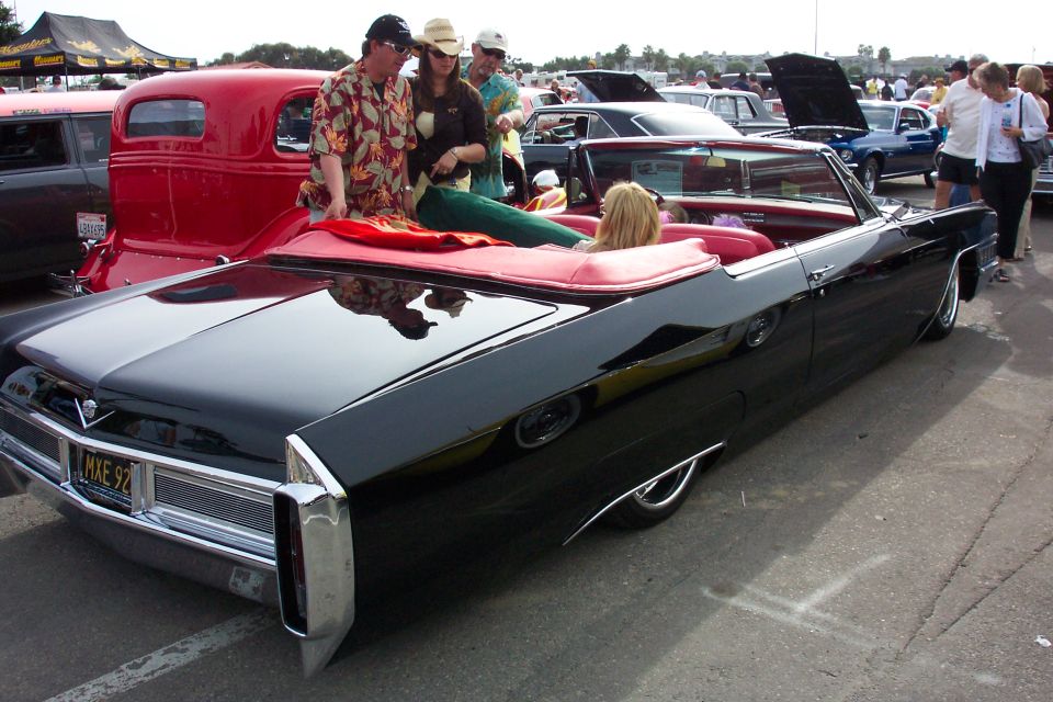 Black mid-60s Cadillac convertible with red interior, people seated on the back, at car show