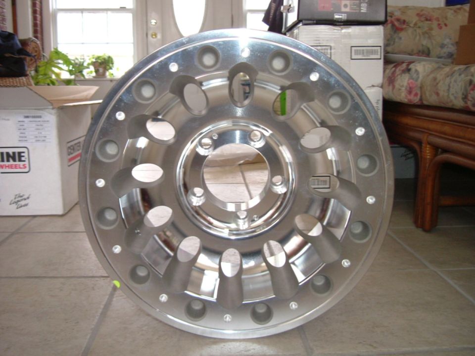 Polished aluminum alloy wheel with oval openings standing upright on tile floor indoors