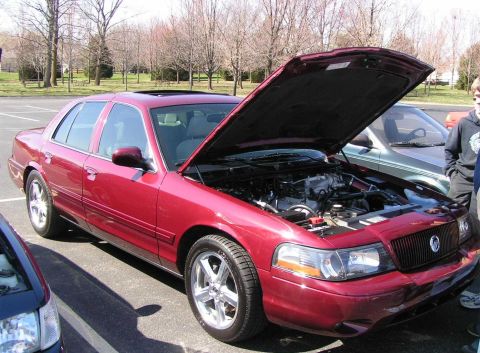 1998 Ford Crown Victoria - A red 1998 Ford Crown Victoria is shown with its hood open, parked in a lot with other vehicles.