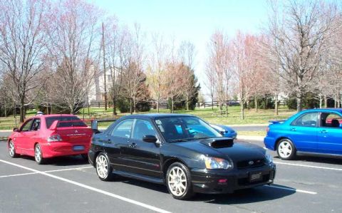 1998 Ford Crown Victoria - A black Subaru WRX STI is parked at a car club meet, with other cars visible in the background.