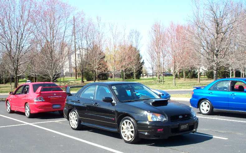 Black Subaru WRX STI parked with a red Mitsubishi Evo and blue Impreza in a parking lot