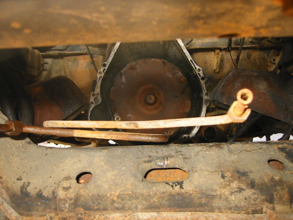 Underside of Bronco showing exposed flexplate with transmission removed and rusty crossmember
