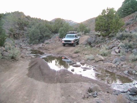 1978 Ford Bronco - A 1978 Ford Bronco navigates a challenging off-road path with puddles and rocks.