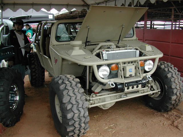 Olive military-style buggy with open hood, exposed radiator and large off-road tires indoors