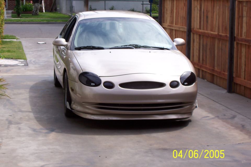 Tan sedan with blacked-out headlights and custom grille, front view