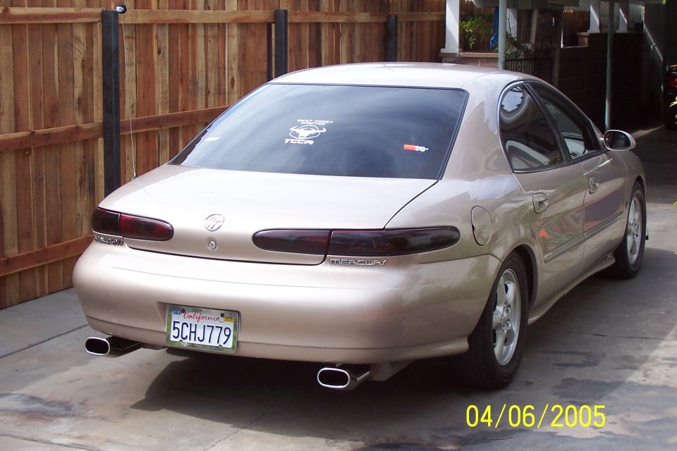 Tan sedan's rear view, showing dual exhaust tips, Mercury badging, and a California license plate