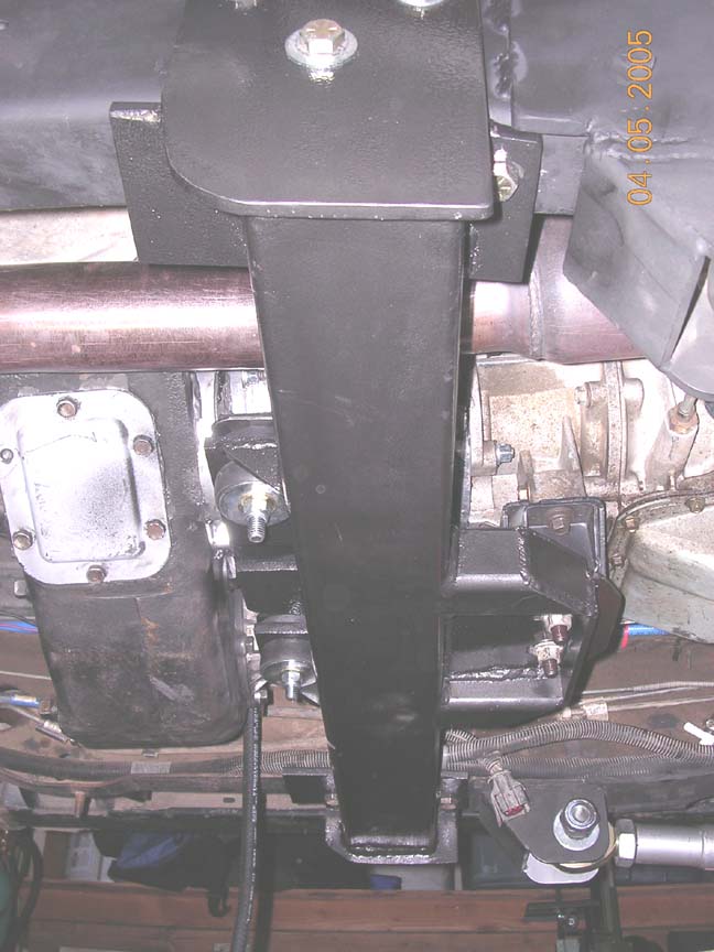 Black fabricated transmission crossmember bolted under a truck beside transfer case and exhaust