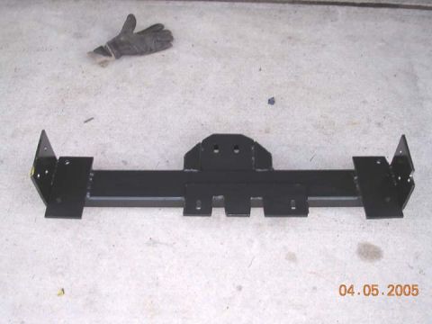 1994 Ford Bronco - A black metal doubler crossmember part is shown on a concrete surface, with a pair of gloves in the background.