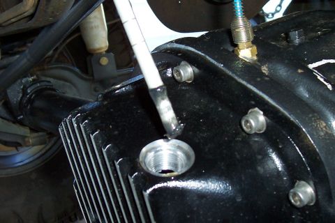 1994 Ford F-150 - A tool is inserted into the fill hole of a differential housing, with a shock absorber visible in the background.