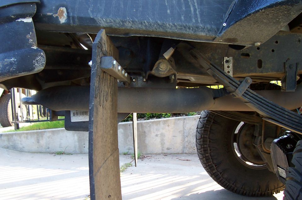 Underside of lifted truck on a wood post showing muffler, leaf springs and rear tire