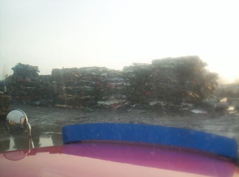 1995 Ford Bronco - Junkyard scene with a large pile of crushed vehicles under a hazy sky.