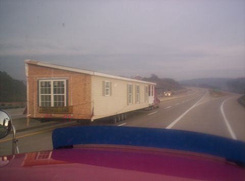 1995 Ford Bronco - A mobile home is being transported down a highway, likely during the day.