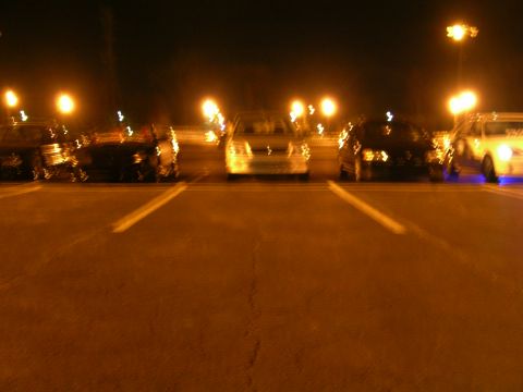 1994 Ford Probe - A line of vehicles are parked in a lot at night, illuminated by overhead lights.